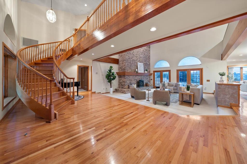A spacious living room features a curved wooden staircase, hardwood floors, and a brick fireplace — 220 HARBOR VIEW LANE, LARGO, FL