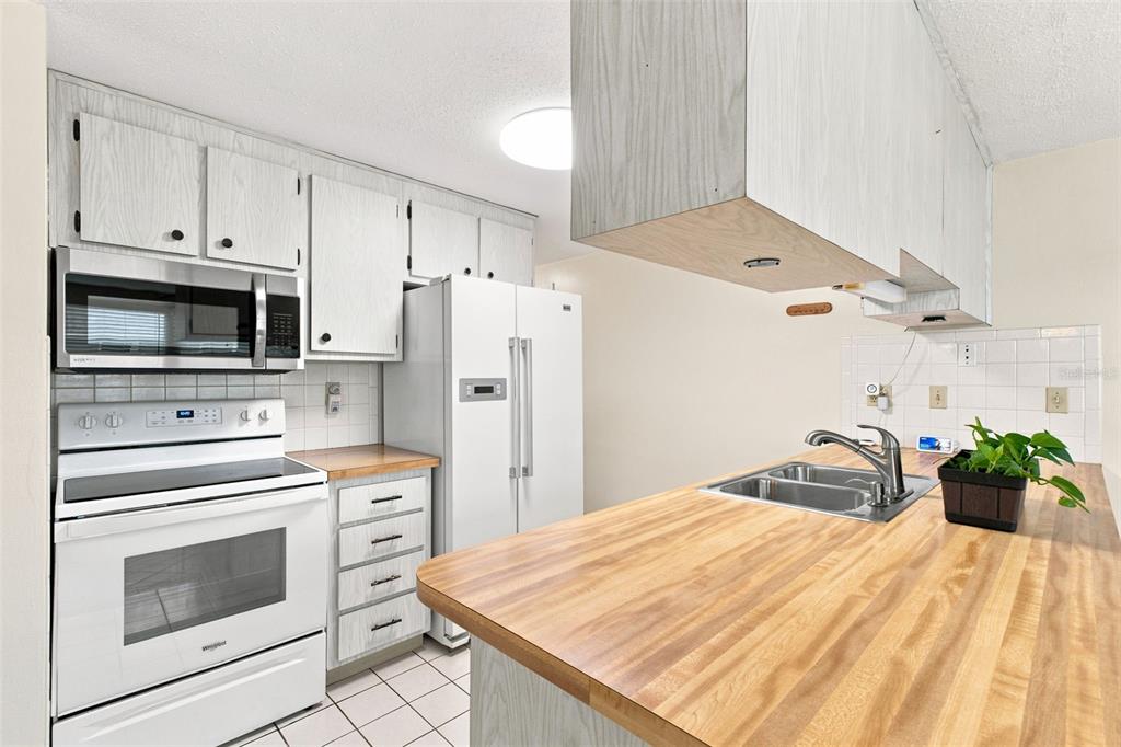 A kitchen features white cabinets, a white stove, a refrigerator, and a wood-look countertop — 7203 CHERRY LAUREL DRIVE, PORT RICHEY, FL