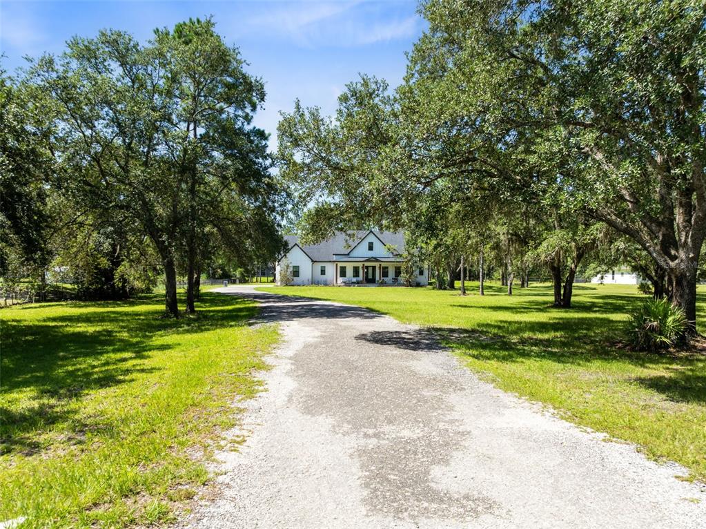 A gravel driveway leads to a white house surrounded by large, mature oak trees — 19110 SHELDON STREET, ORLANDO, FL