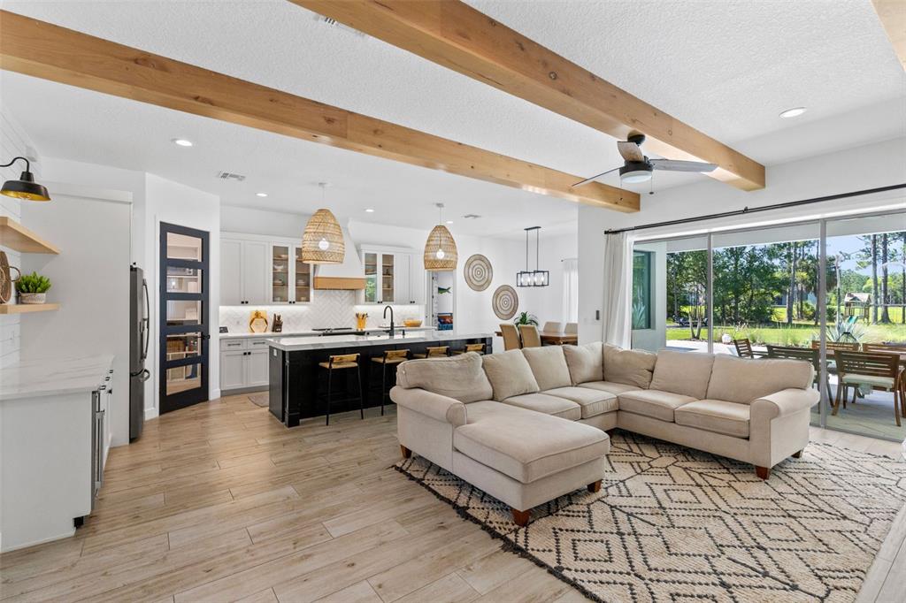 An open-concept living room and kitchen feature wood ceiling beams, a sectional sofa, and patio access — 19110 SHELDON STREET, ORLANDO, FL