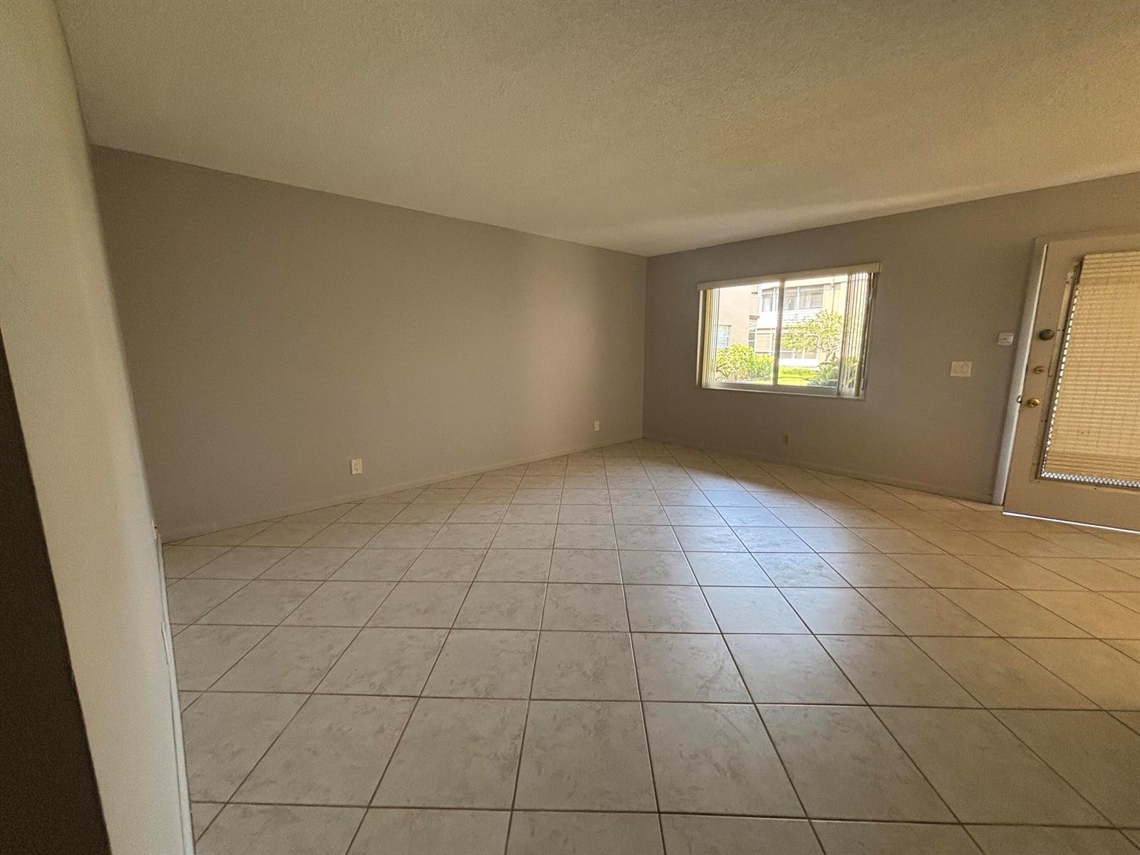 An empty living room with light-colored tile flooring, gray walls, a window, and a door — 341 Piedmont # H, Delray Beach FL 33484, DELRAY BEACH, FL