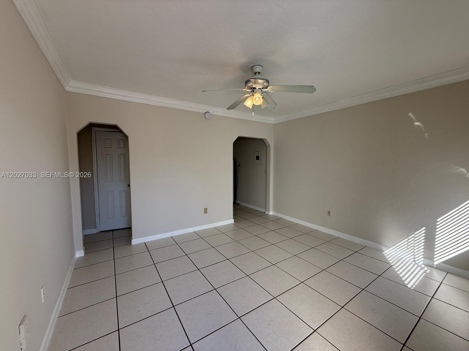 An empty room features beige walls, white crown molding, and light-colored square floor tiles — MIAMI, FL