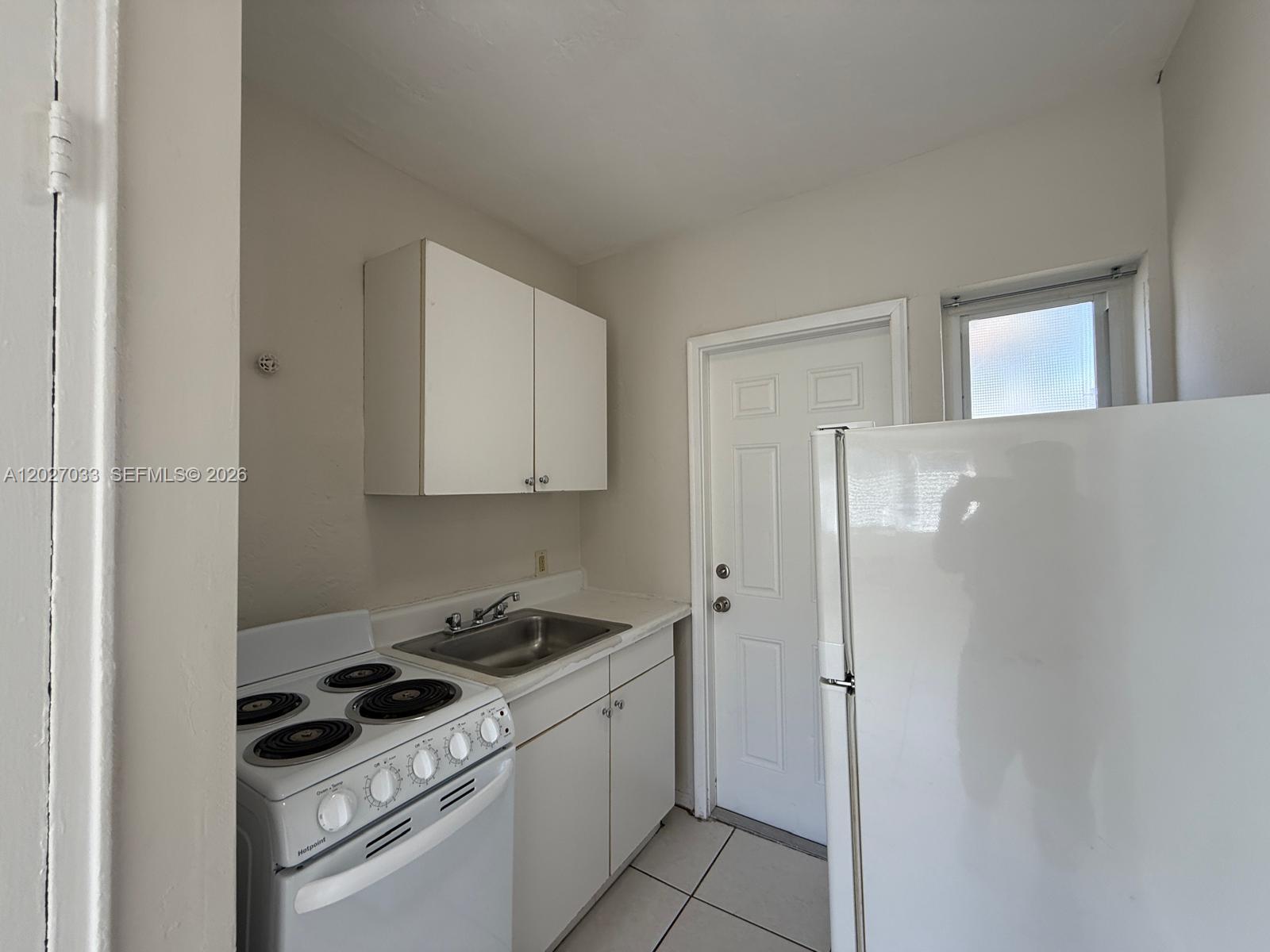 A small kitchen features white cabinets, a stove, a sink, and a refrigerator — MIAMI, FL