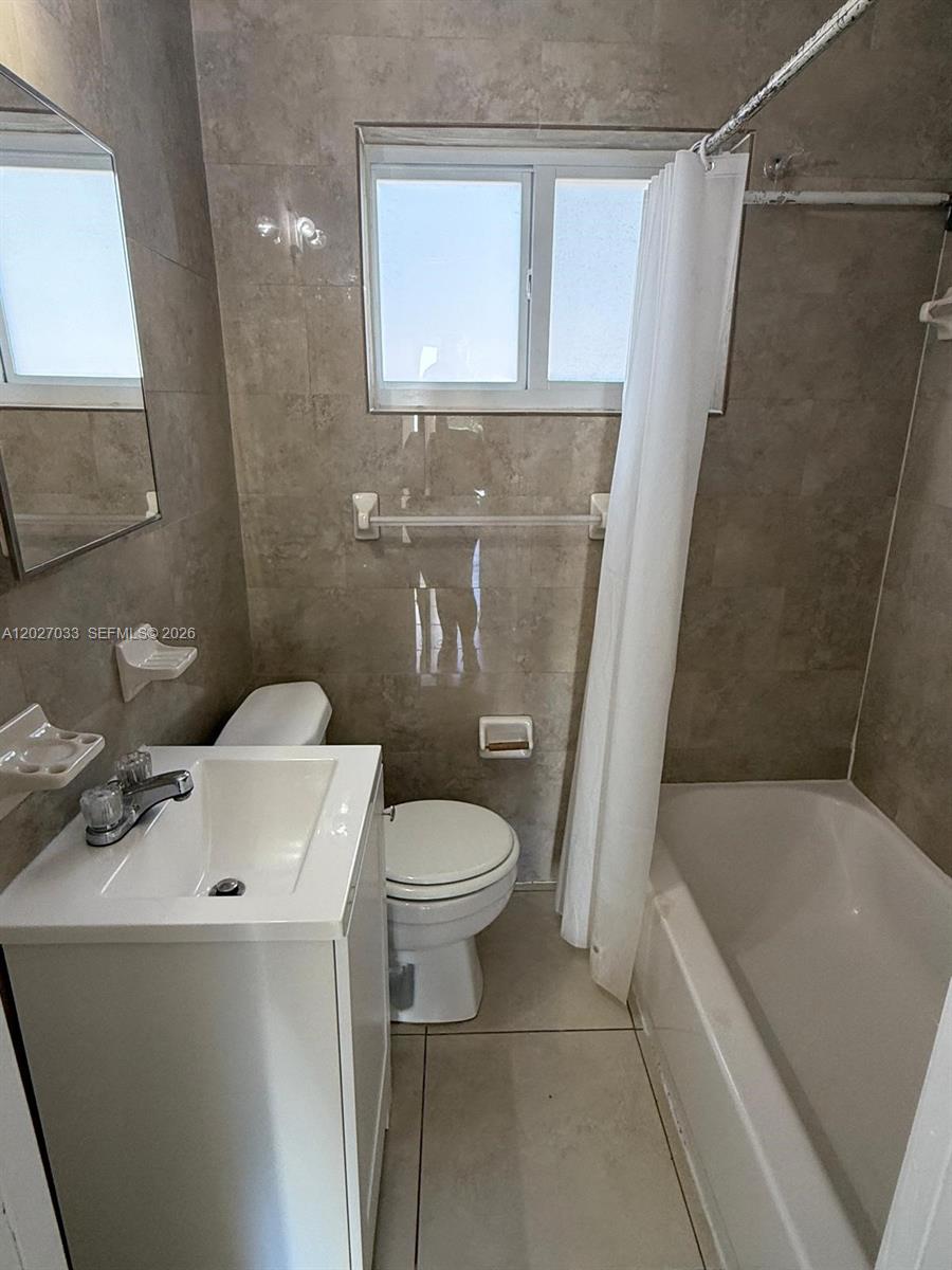 A small bathroom features a white vanity, a toilet, and a tiled bathtub shower combination — MIAMI, FL