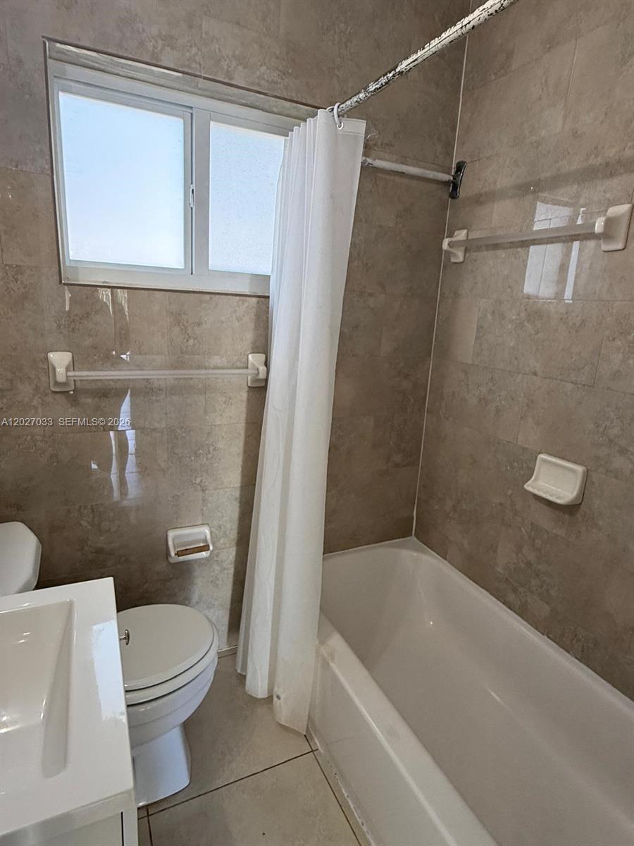 A bathroom features a white toilet, a vanity, and a tiled bathtub with a shower curtain — MIAMI, FL