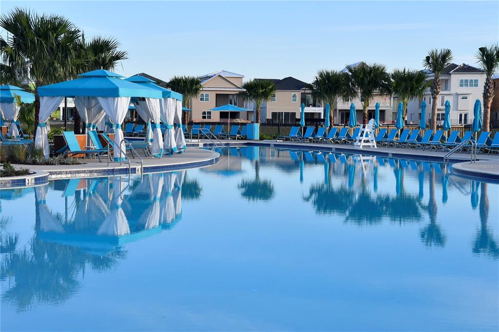 A swimming pool with lounge chairs and cabanas sits in front of multi-story houses — 2956 ON THE ROCKS, KISSIMMEE, FL