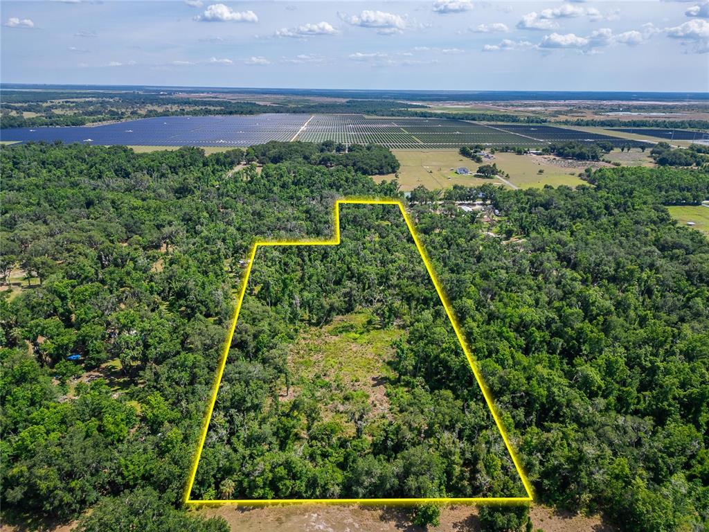 An aerial view shows a wooded plot of land outlined in yellow near a solar farm — 672 HIGHWAY, LITHIA, FL