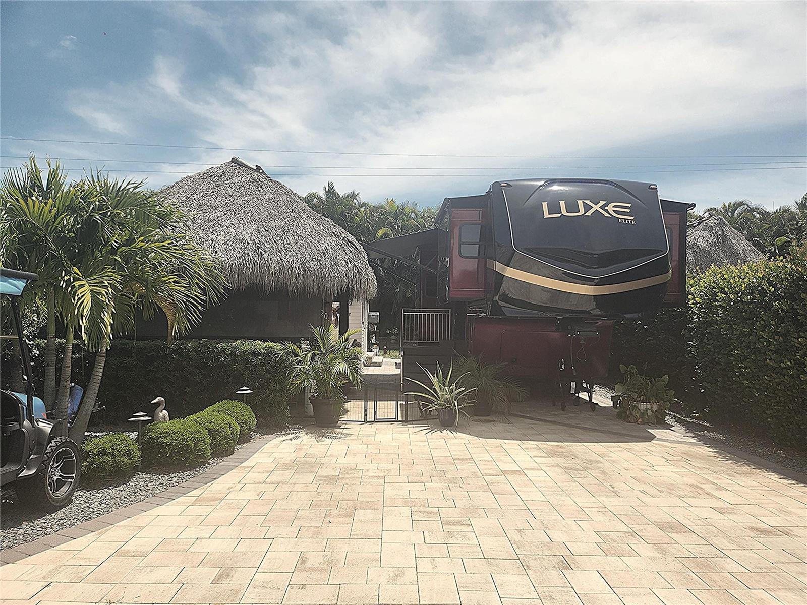 A Luxe Elite fifth-wheel trailer is parked on a paved driveway next to a tiki hut — 622 SW 42nd Cove, Okeechobee FL 34974, OKEECHOBEE, FL