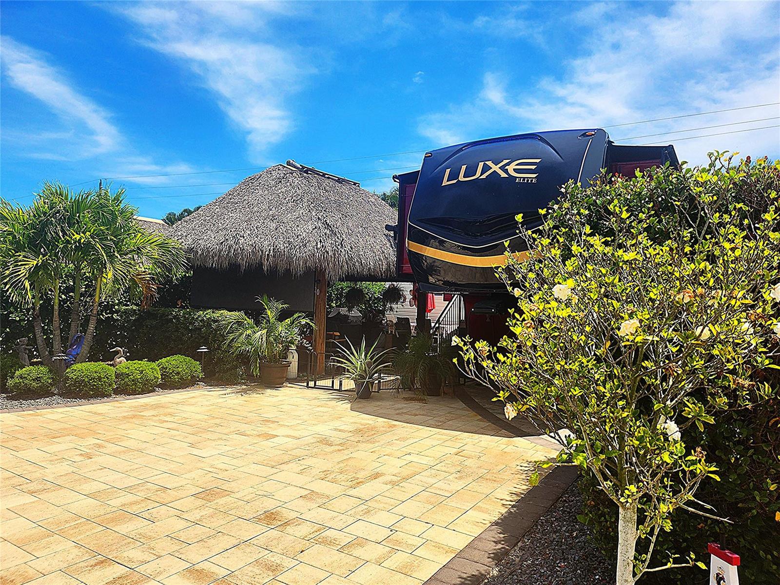 A Luxe Elite fifth-wheel trailer is parked on a paved patio next to a tiki hut — 622 SW 42nd Cove, Okeechobee FL 34974, OKEECHOBEE, FL