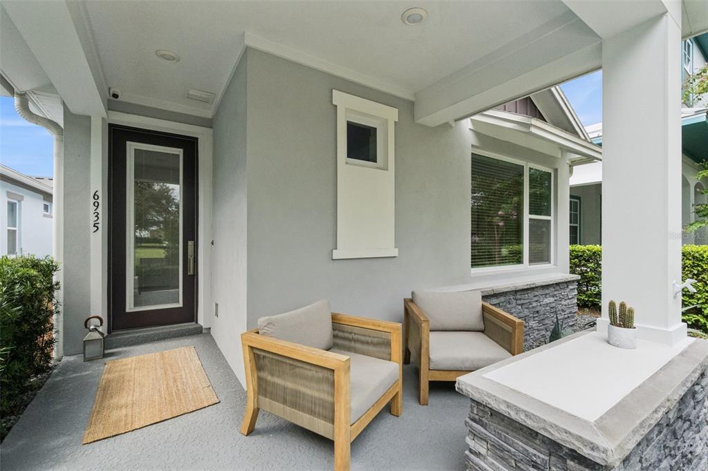 A covered front porch features two wooden armchairs, a rug, and a stone-accented wall — 6935 HIGGS ALLEY, ORLANDO, FL