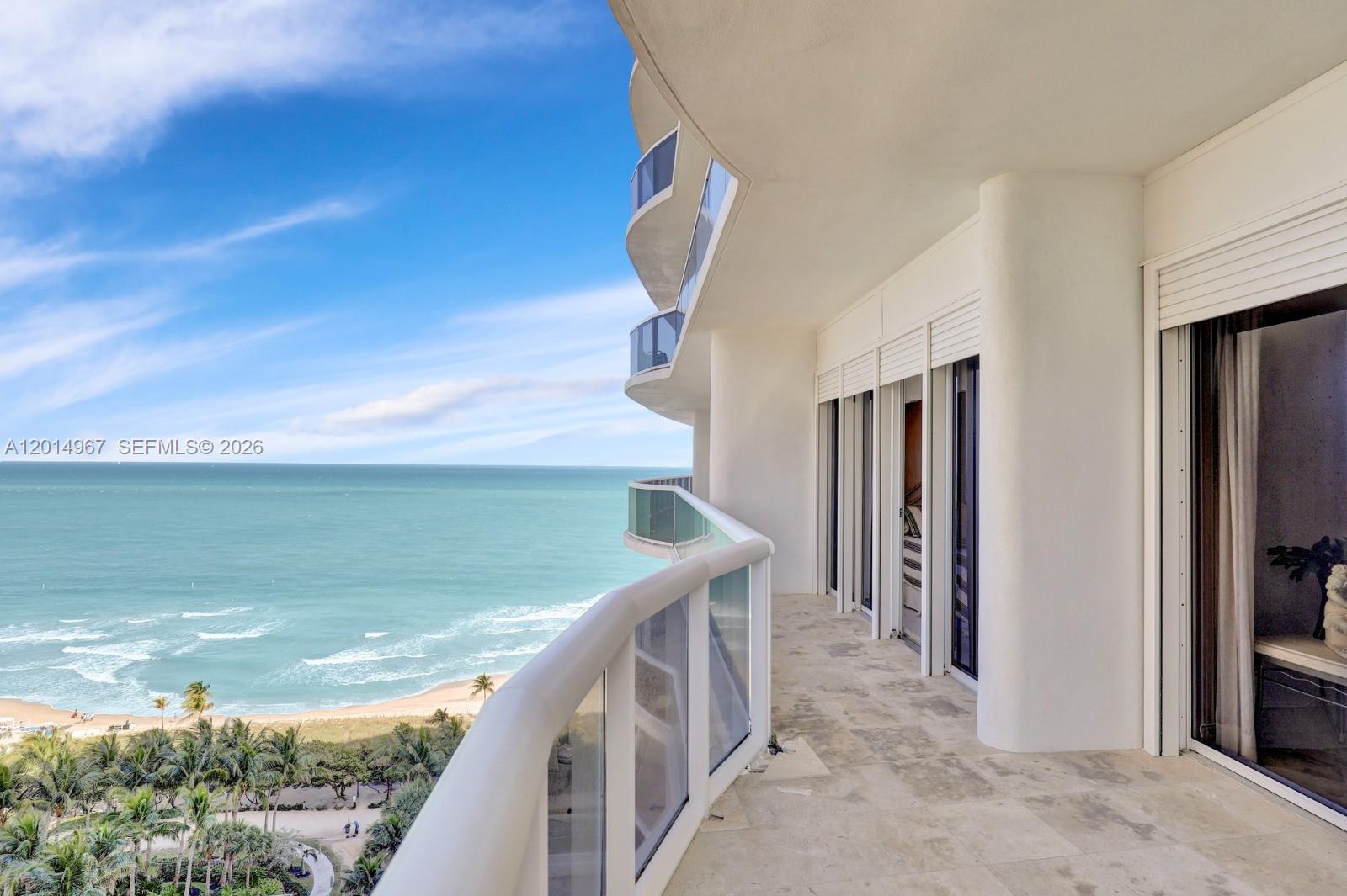A curved balcony with glass railings overlooks the ocean and a beach with palm trees — 9601 Collins Ave # 1502, Bal Harbour FL 33154, BAL HARBOUR, FL