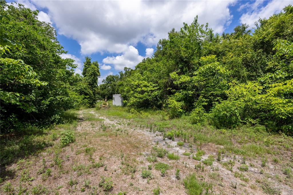 A dirt path leads through a wooded area toward a small, light-colored utility structure — 3728 N US HIGHWAY 441, OCALA, FL
