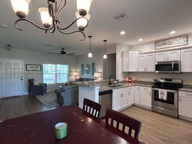 This open-concept kitchen features white cabinetry, stainless steel appliances, and a dining area with a chandelier — 109 Vale Cr, Sebring FL 33876, SEBRING, FL