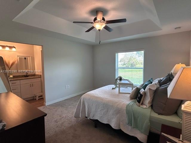 A bedroom with a tray ceiling, ceiling fan, carpeted floor, and an attached bathroom — 109 Vale Cr, Sebring FL 33876, SEBRING, FL