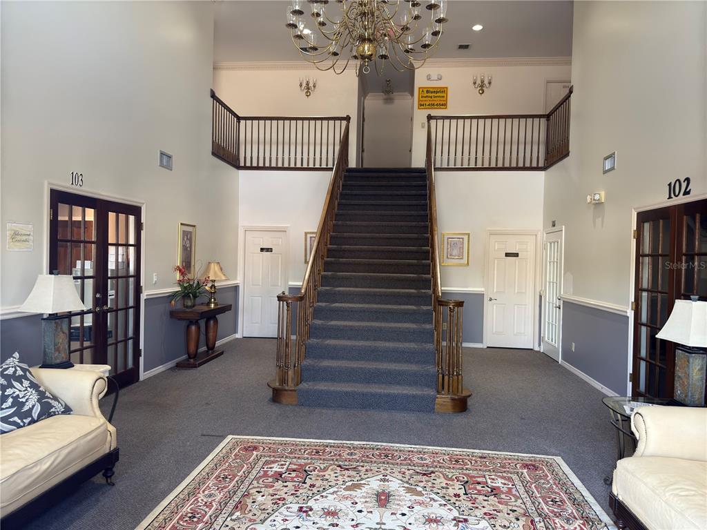 A grand foyer features a central staircase, a large chandelier, and doors labeled 102 and 103 — 949 TAMIAMI TRAIL UNIT 102, PORT CHARLOTTE, FL