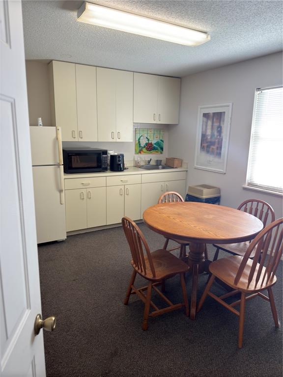 A small kitchen features off-white cabinets, a round wooden table, and carpeted flooring — 949 TAMIAMI TRAIL UNIT 102, PORT CHARLOTTE, FL