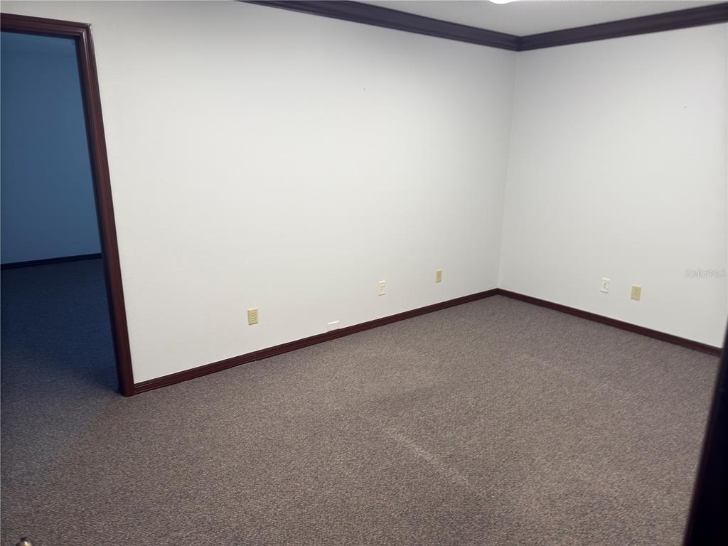 An empty room with white walls, dark wood trim, and gray carpeted flooring — 949 TAMIAMI TRAIL UNIT 102, PORT CHARLOTTE, FL