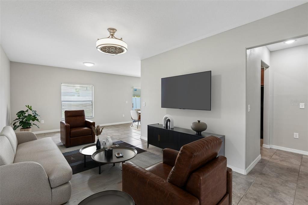 A living room features a grey sofa, two brown leather armchairs, and a wall-mounted television — 7414 CLARY SAGE AVENUE, TAMPA, FL