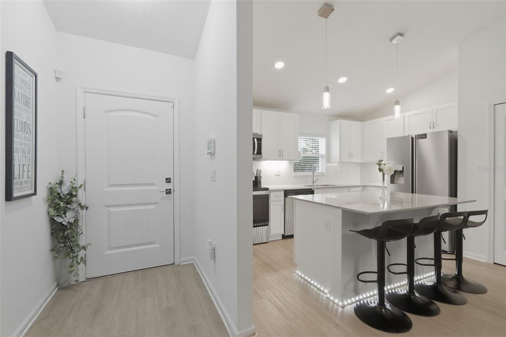 A white kitchen with an island and bar stools is visible from a home entryway — 1 SERVICE TREE PLACE, PALM COAST, FL