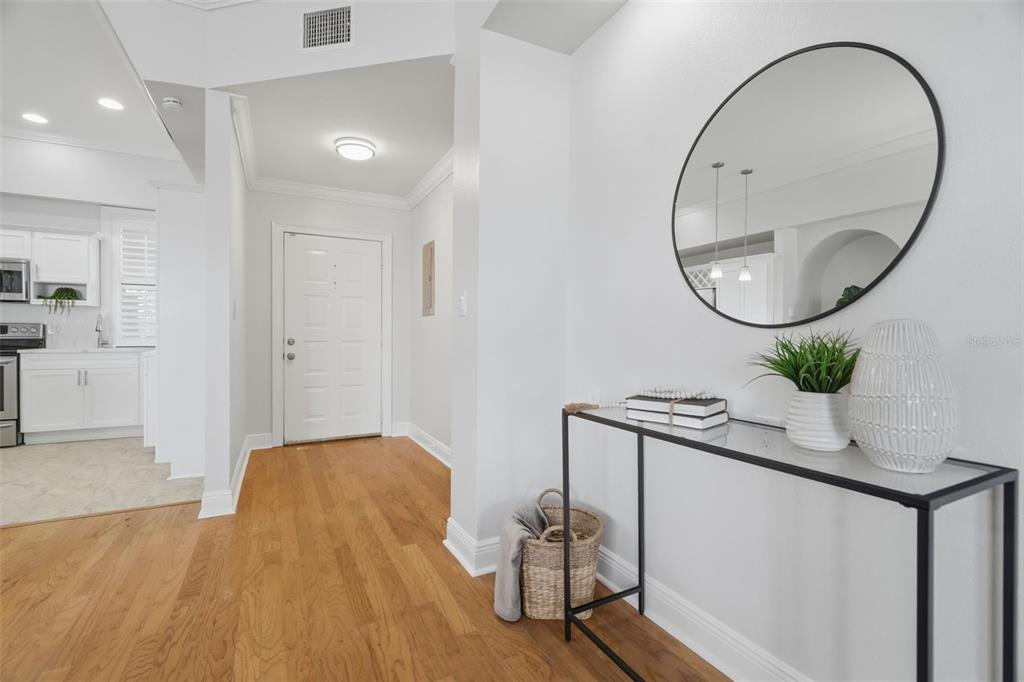 An entryway features hardwood floors, a glass-topped console table, a round mirror, and a door — 3127 W SLIGH AVENUE UNIT 203B, TAMPA, FL