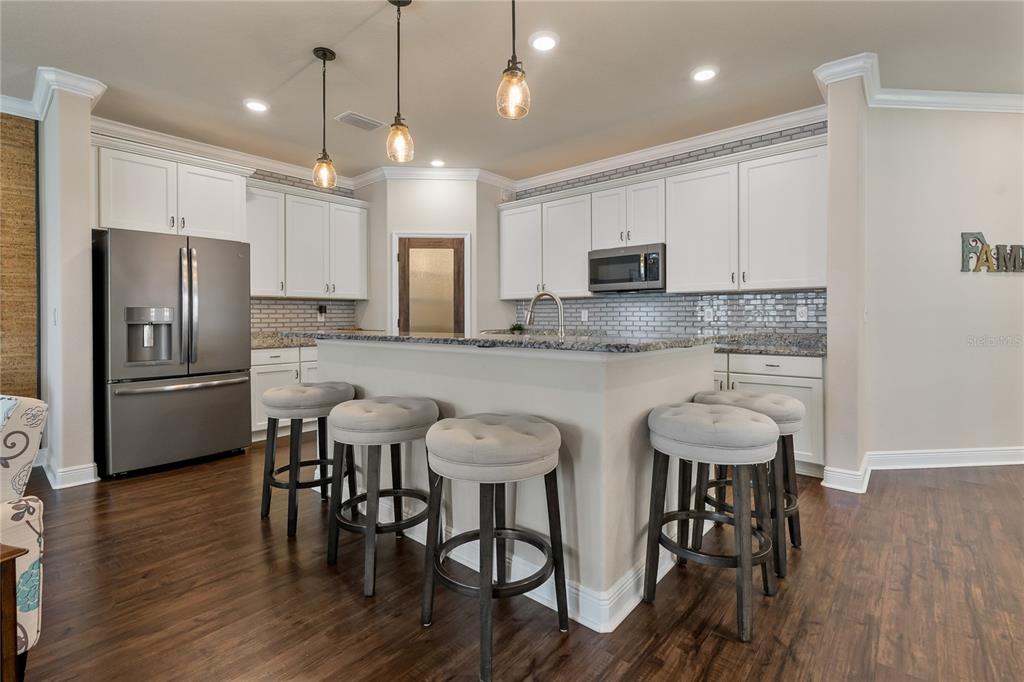 A kitchen features white cabinetry, granite countertops, a central island with bar stools, and flooring — 597 OZONA VILLAGE DRIVE, PALM HARBOR, FL