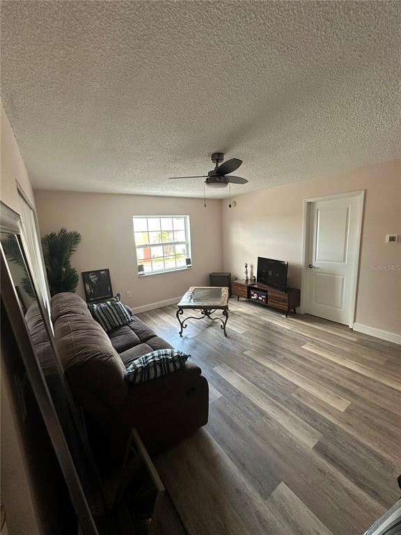 A living room features light walls, wood-look flooring, a ceiling fan, and a glass coffee table — 1084 82ND TERRACE N UNIT 1084E, ST PETERSBURG, FL