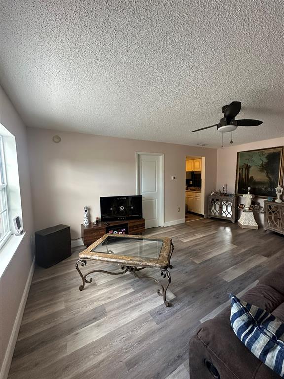 A living room features wood-look flooring, a ceiling fan, a glass-top coffee table, and television — 1084 82ND TERRACE N UNIT 1084E, ST PETERSBURG, FL