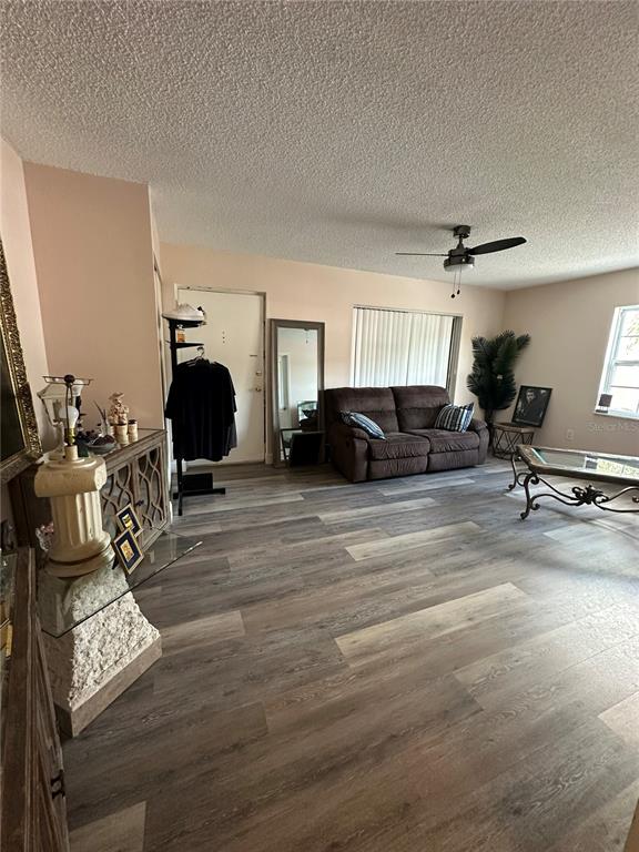 A living room features wood-look flooring, a brown loveseat, a ceiling fan, and a mirror — 1084 82ND TERRACE N UNIT 1084E, ST PETERSBURG, FL