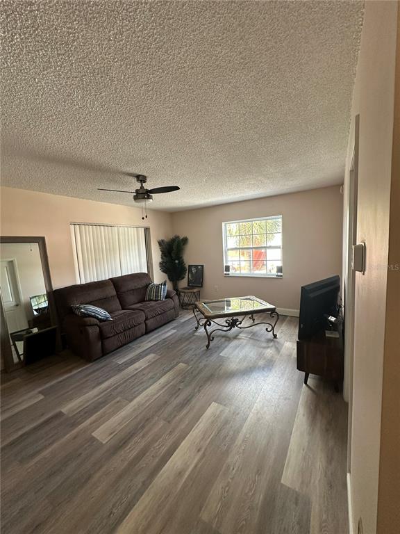 A living room with wood-look flooring, a brown sofa, a coffee table, and a ceiling fan — 1084 82ND TERRACE N UNIT 1084E, ST PETERSBURG, FL