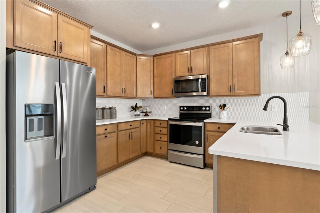 A kitchen with wood cabinets, stainless steel appliances, white countertops, and a tile backsplash — 4600 ORCHARD VIEW ALLEY, CLERMONT, FL