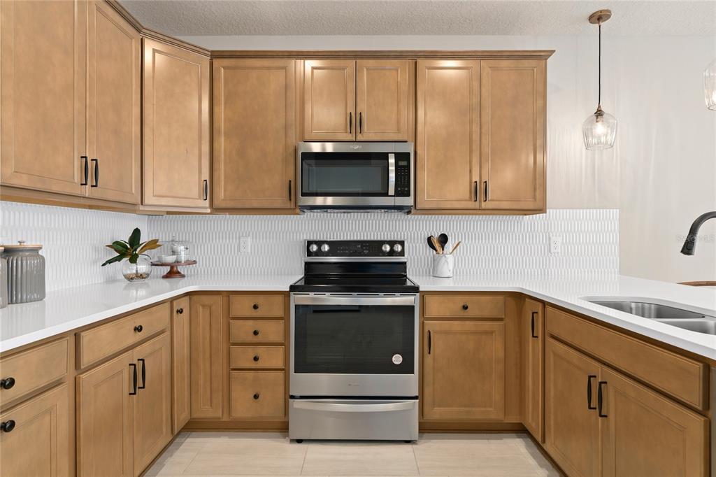 A kitchen features light wood cabinets, stainless steel appliances, white countertops, and a textured backsplash — 4600 ORCHARD VIEW ALLEY, CLERMONT, FL