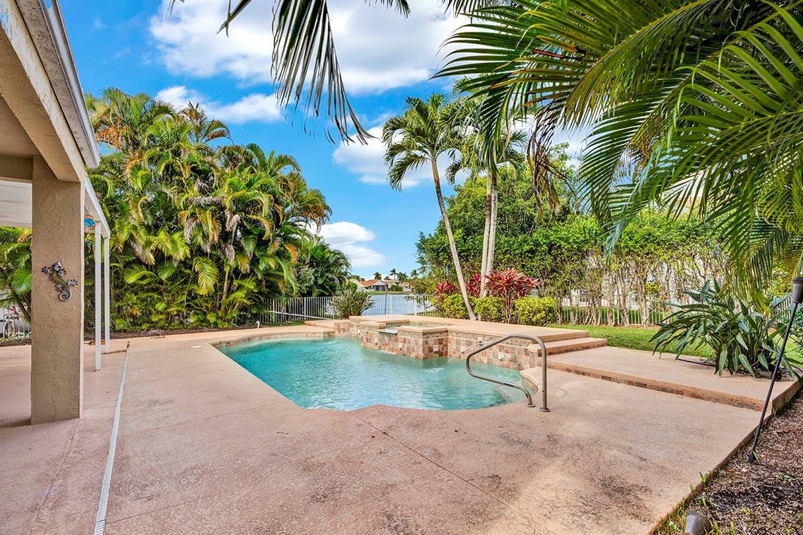 A swimming pool with a raised spa sits on a concrete patio beside palm trees — 19571 Black Olive Lane, Boca Raton FL 33498, BOCA RATON, FL