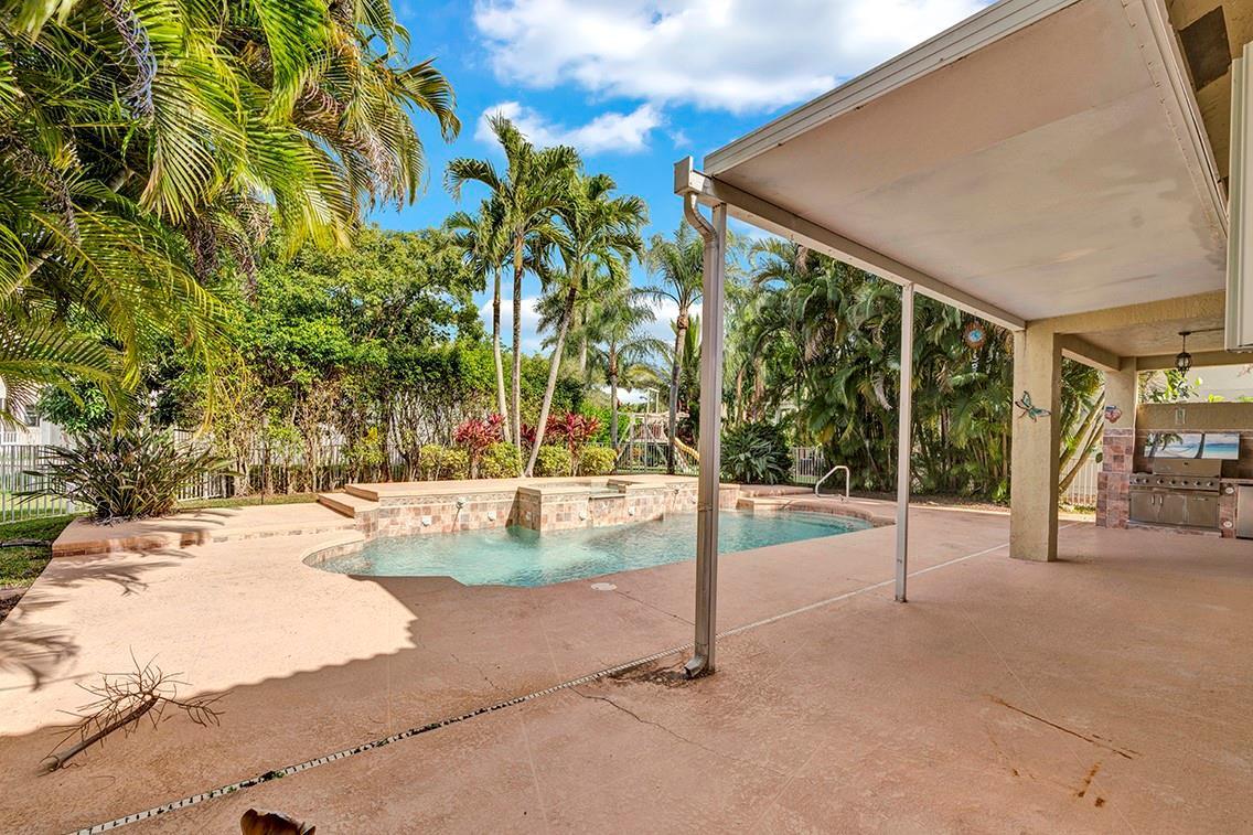 A backyard patio features a swimming pool, a raised spa, and an outdoor kitchen area — 19571 Black Olive Lane, Boca Raton FL 33498, BOCA RATON, FL