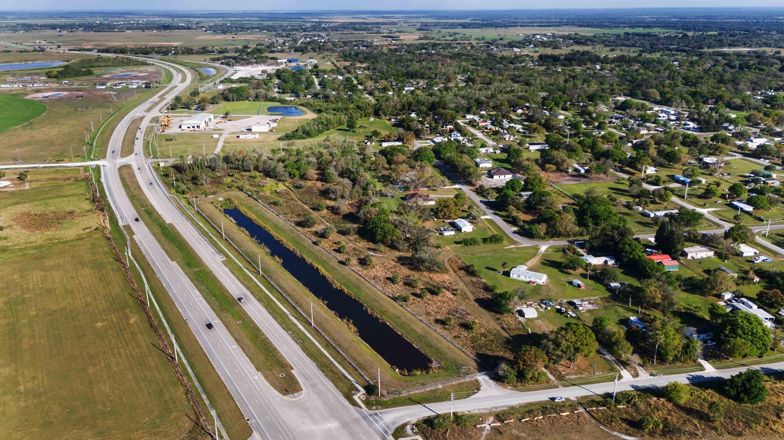 An aerial view shows a highway running alongside a long drainage canal and residential neighborhood — 0 NE 60th & 64th Avenue, Okeechobee FL 34974, OKEECHOBEE, FL