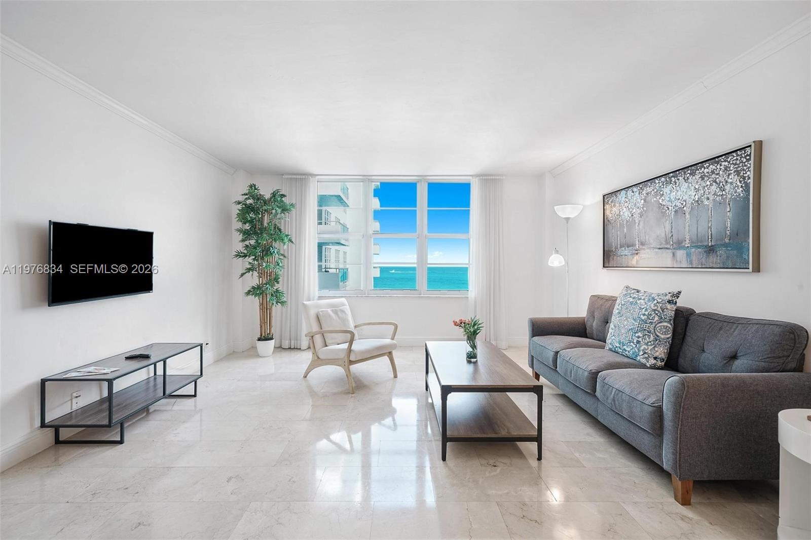 A living room features a gray sofa, a coffee table, a television, and ocean views — 5101 Collins Ave # 11L, Miami Beach FL 33140, MIAMI BEACH, FL