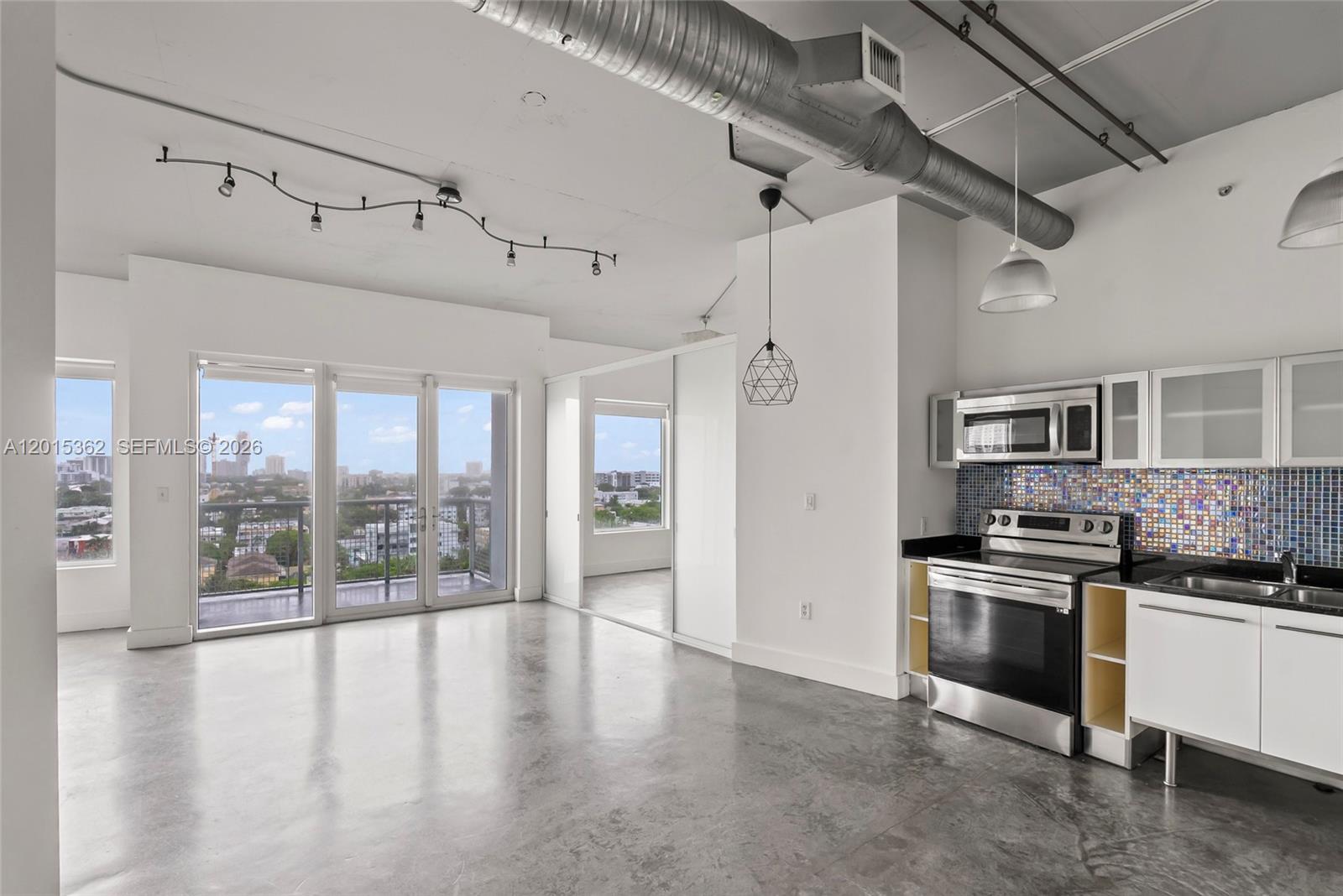 An open-concept apartment features a kitchen with stainless steel appliances, concrete floors, and balcony access — 10 SW South River Dr # 1006, Miami FL 33130, MIAMI, FL