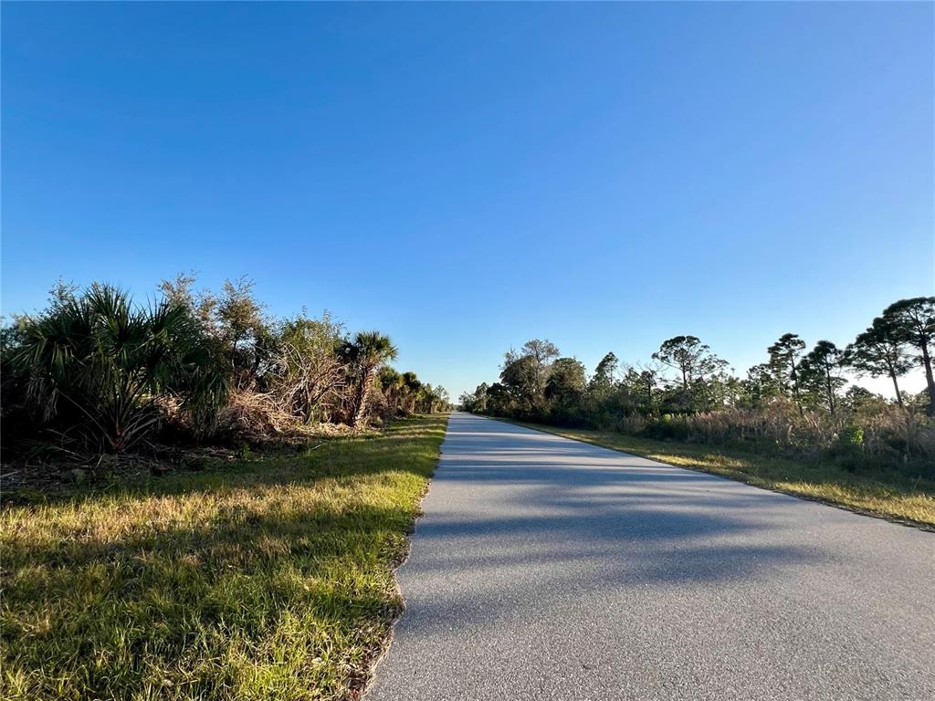 A paved road stretches through a grassy landscape with trees under a clear blue sky — 14113 MAGNESS AVENUE, PORT CHARLOTTE, FL