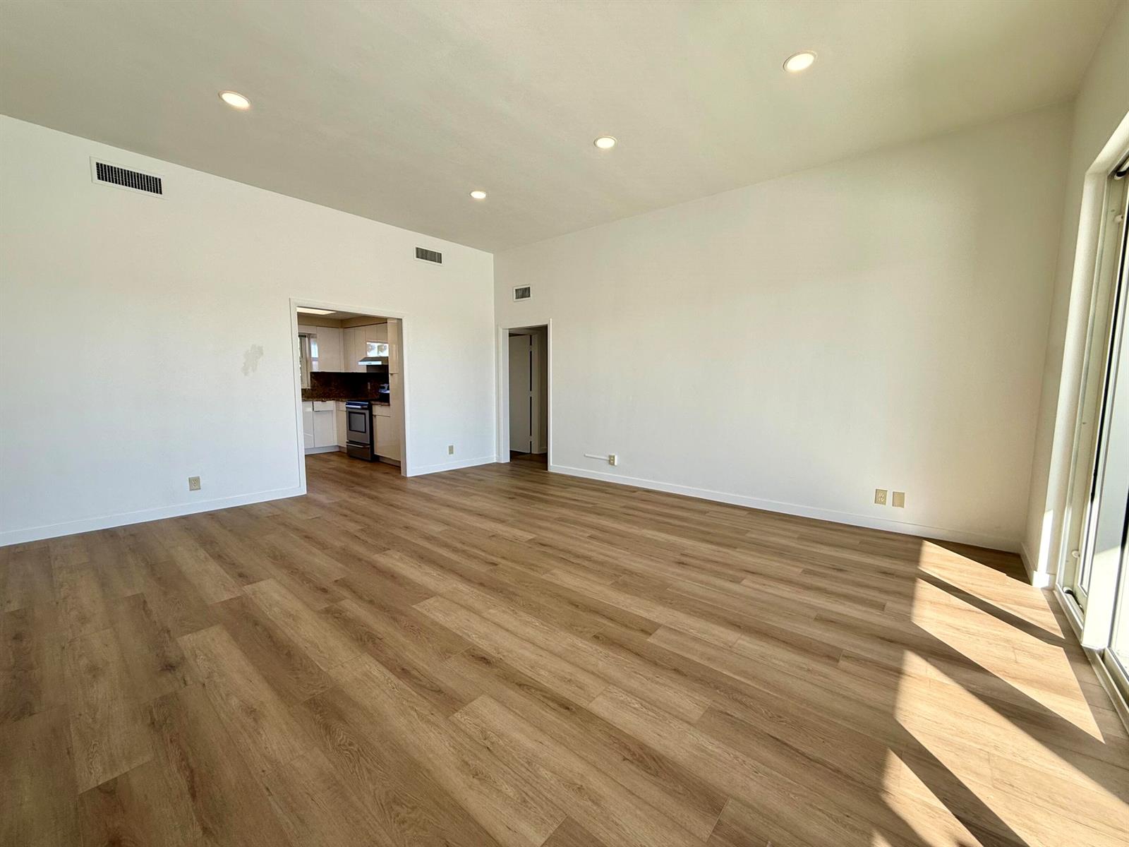 An empty room with light wood-look flooring, white walls, recessed lighting, and a kitchen doorway — 1165 E Atlantic Avenue # A, Delray Beach FL 33483, DELRAY BEACH, FL