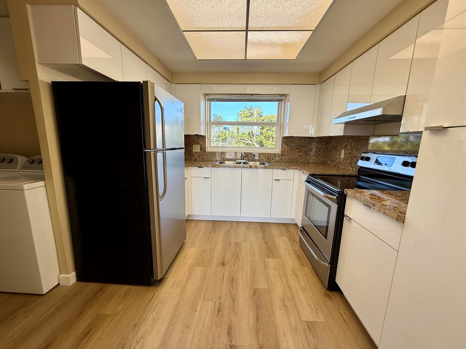 A kitchen features white cabinets, stainless steel appliances, granite countertops, and light wood-look flooring — 1165 E Atlantic Avenue # A, Delray Beach FL 33483, DELRAY BEACH, FL