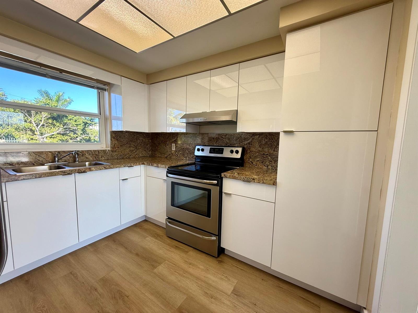 A kitchen features white flat-panel cabinets, granite countertops, stainless steel appliances, and wood-look flooring — 1165 E Atlantic Avenue # A, Delray Beach FL 33483, DELRAY BEACH, FL