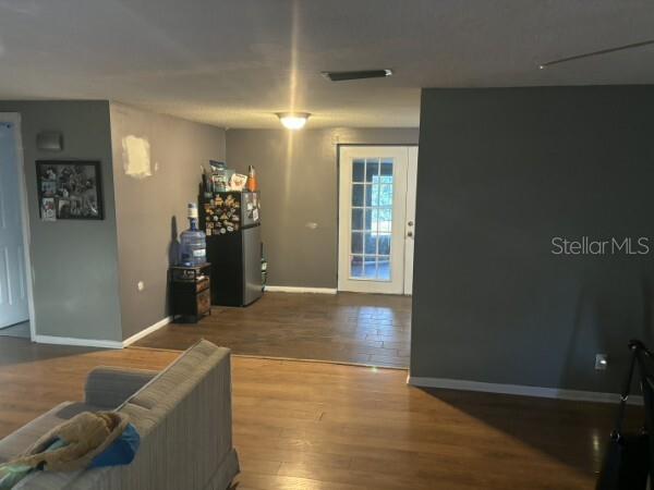 A living room with wood-look flooring leads to a kitchen area with a refrigerator — 4801 AVON STREET, LAKE WALES, FL