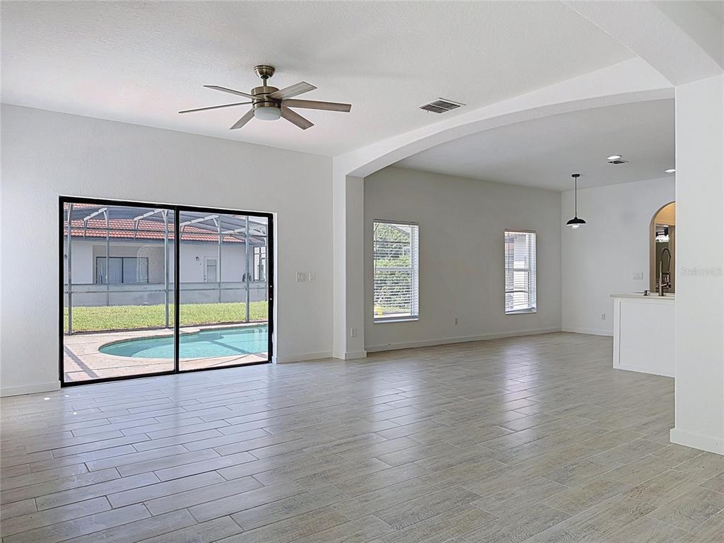 A spacious living area with light tile flooring, a ceiling fan, and sliding glass doors — 16710 CARIBBEAN BREEZE WAY, CLERMONT, FL