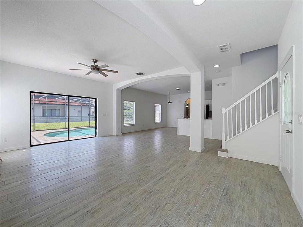 An open-concept living area features light wood-look tile floors, a staircase, and sliding glass doors — 16710 CARIBBEAN BREEZE WAY, CLERMONT, FL