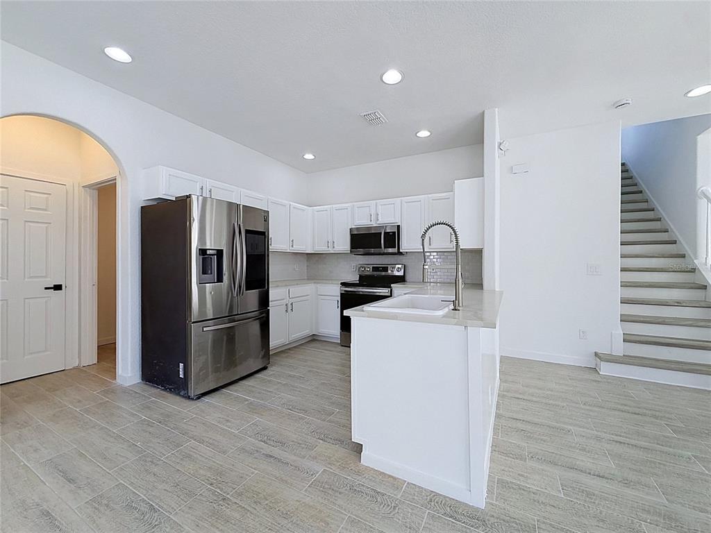 A modern kitchen features white cabinets, stainless steel appliances, a center island, and tile flooring — 16710 CARIBBEAN BREEZE WAY, CLERMONT, FL