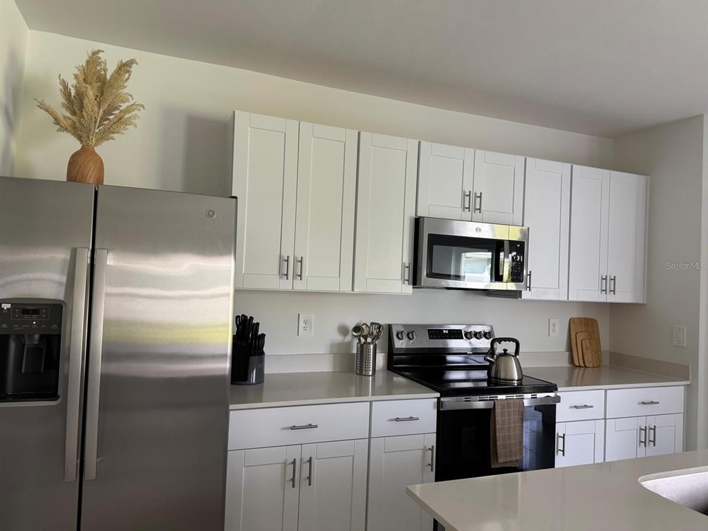 A kitchen features white cabinets, stainless steel appliances, and light-colored countertops — 7111 WEEPING PINE DRIVE, FORT MYERS, FL