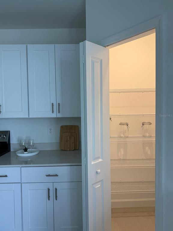 A white kitchen cabinet and countertop area next to an open pantry with wire shelving — 7111 WEEPING PINE DRIVE, FORT MYERS, FL