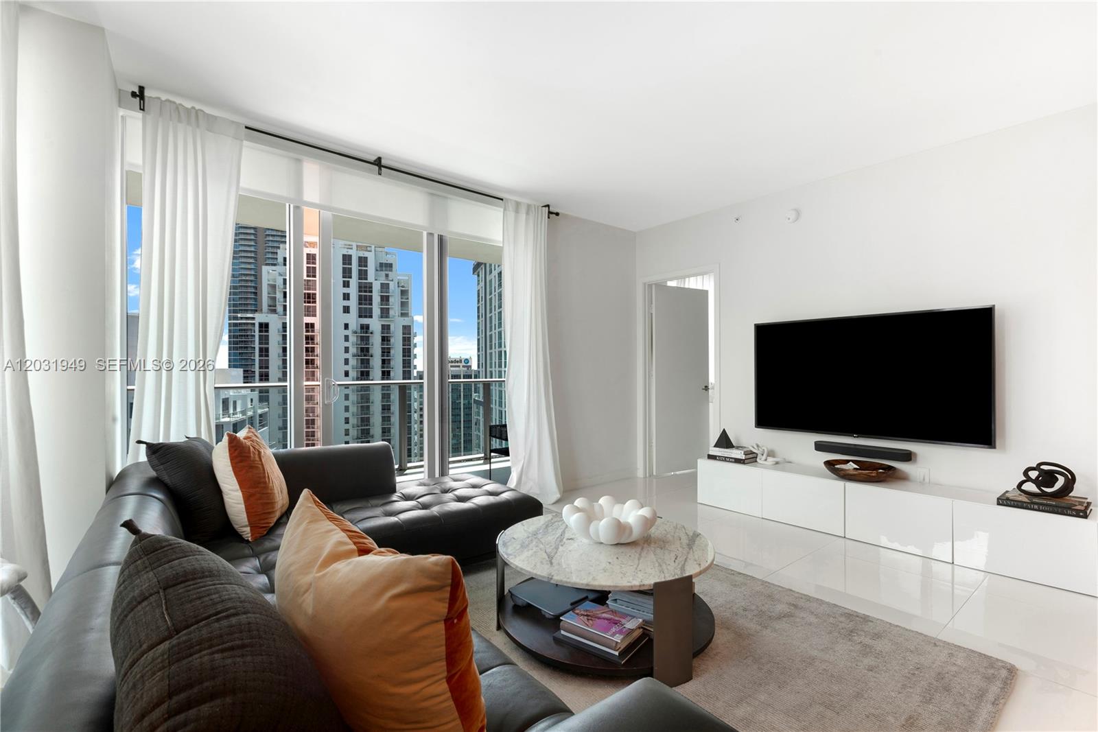 A modern living room features a dark leather sectional, marble coffee table, and floor-to-ceiling windows — 1100 S Miami Ave # 3810, Miami FL 33130, MIAMI, FL