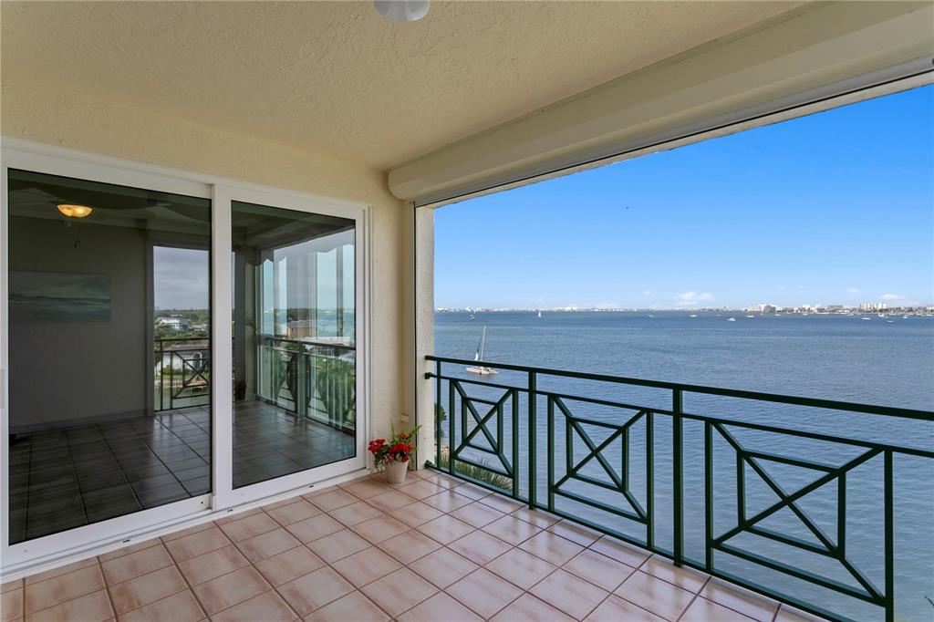A tiled balcony features a green metal railing overlooking a wide bay and distant city — 4717 DOLPHIN CAY LANE S UNIT 507, ST PETERSBURG, FL