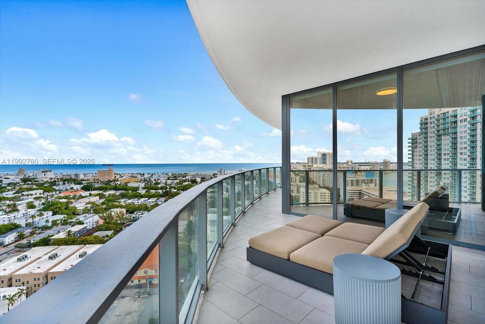 A curved balcony features lounge chairs, glass railings, and panoramic views of the ocean and city — 500 Alton Rd # 2205, Miami Beach FL 33139, MIAMI BEACH, FL
