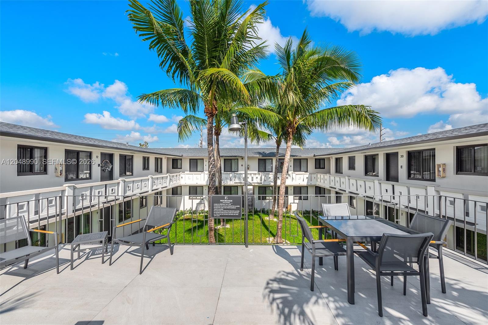 An outdoor rooftop deck features patio furniture, palm trees, and a view of apartment units — 1345 W 28th St # 4, Hialeah FL 33010, HIALEAH, FL
